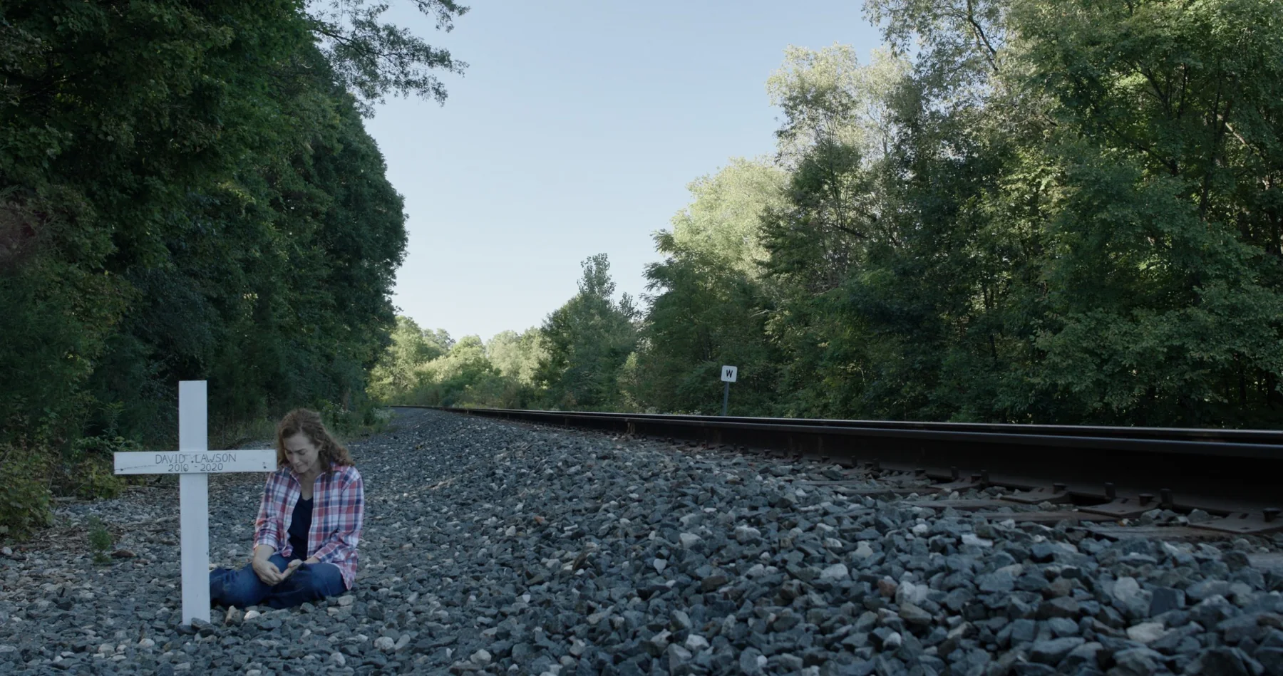 Sonia beside a memorial cross near railroad tracks