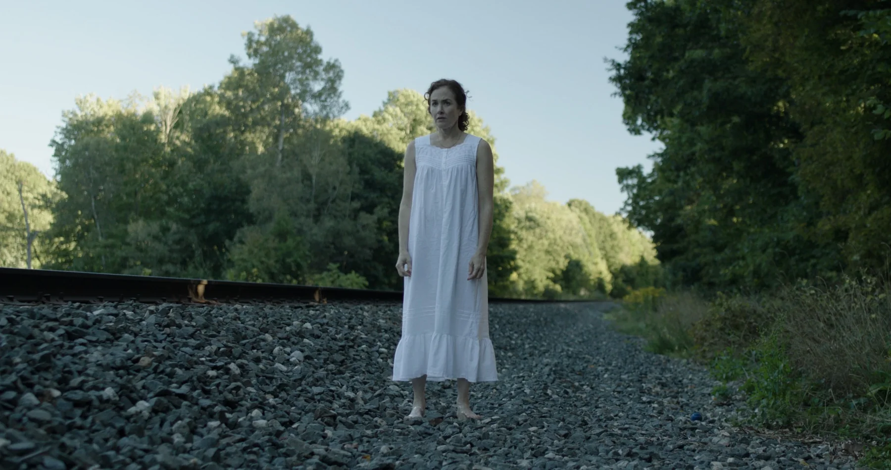 Sonia in a white dress beside railroad tracks