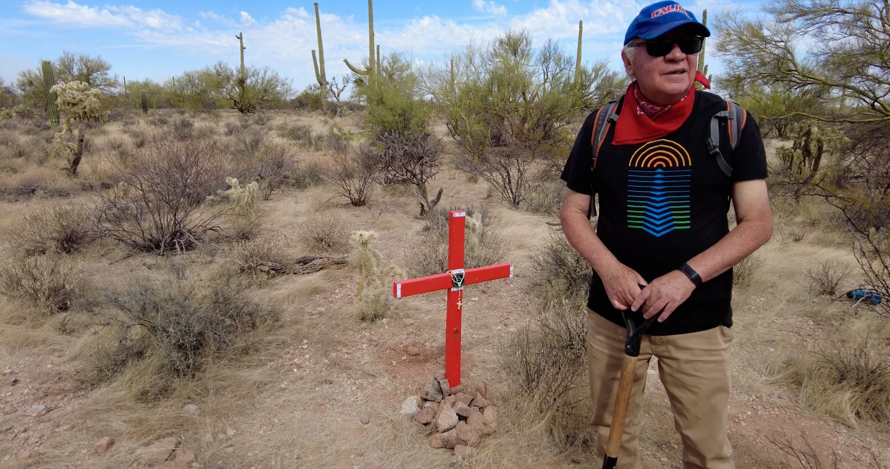 A man standing beside a red cross in the desert