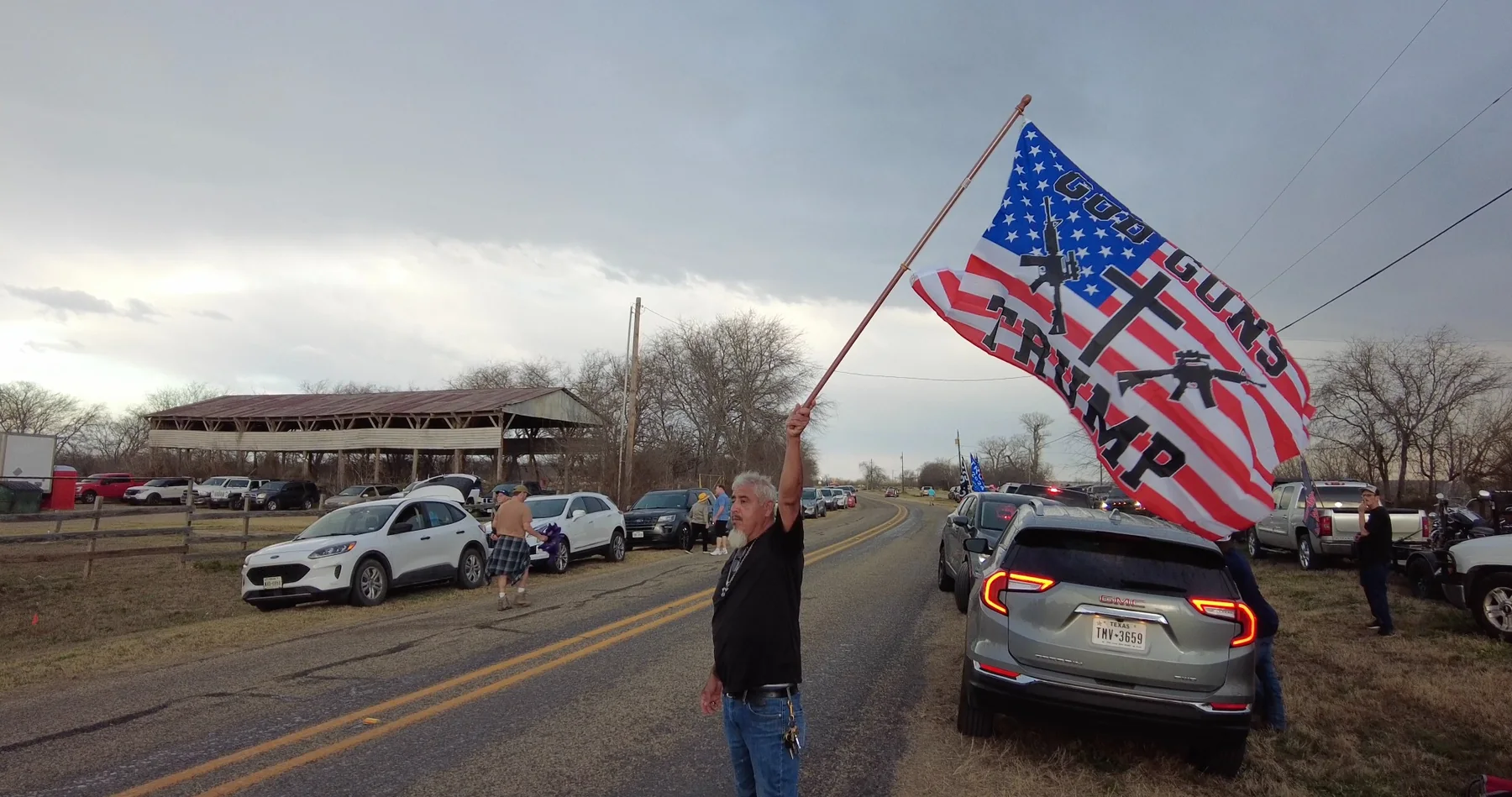 A man holding a flag beside a roadside gathering